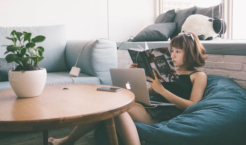 女人坐在豆袋白色，使用macbook在圆桌前与绿色叶子的植物 · 免费素材图片