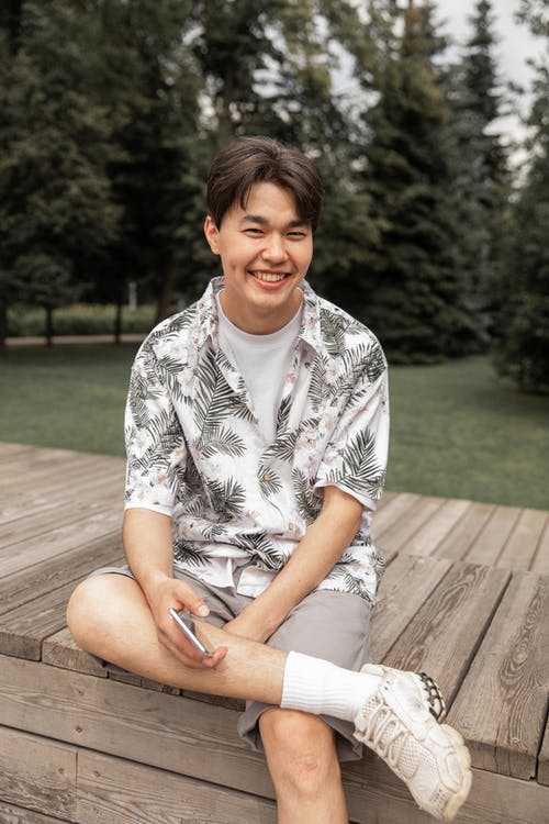 微笑快乐年轻的亚洲男性，而在公园的长凳上冷 · 免费素材图片