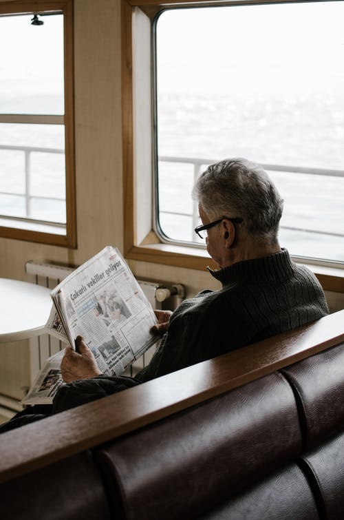 读报纸时坐在长椅上的男人 · 免费素材图片