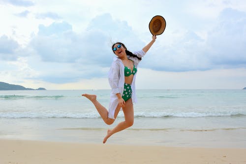 女人在海边跳，拿着帽子 · 免费素材图片