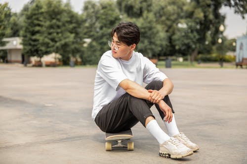 体贴的年轻时尚亚洲人滑板后在公园里休息 · 免费素材图片