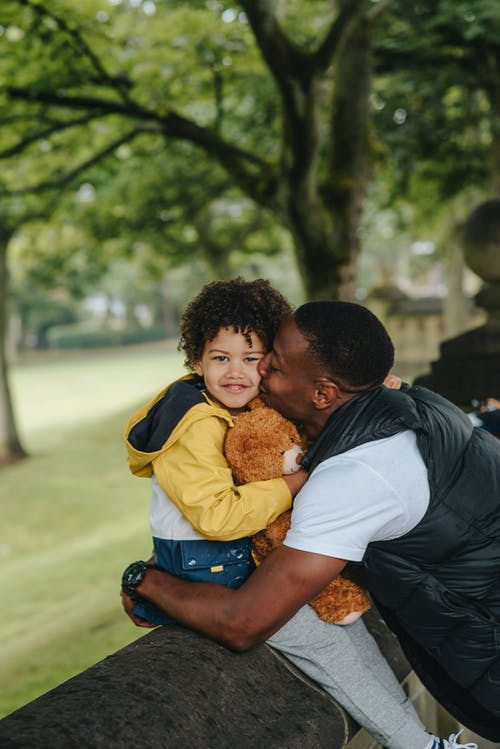 拥抱小儿子的年轻黑人父亲坐在混凝土篱芭 · 免费素材图片