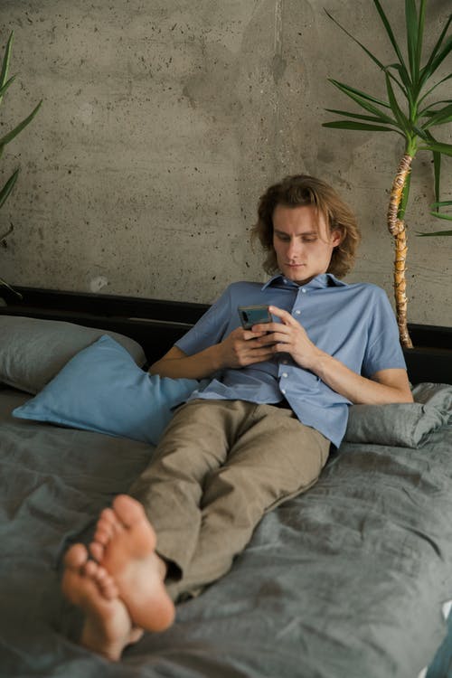 年轻人在床上的浏览智能手机 · 免费素材图片