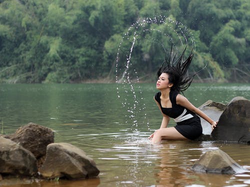 女人坐在水中的岩石 · 免费素材图片