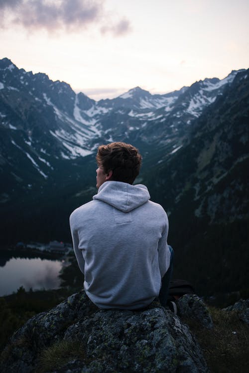 男人穿着白色连帽衫坐在一块岩石上，山上的景色 · 免费素材图片