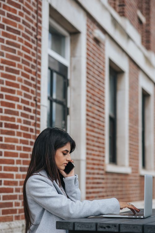 族裔女商人，在户外在笔记本电脑上打字时在智能手机上说 · 免费素材图片