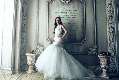 女人穿着白色婚纱站在灰色的墙旁边 · 免费素材图片