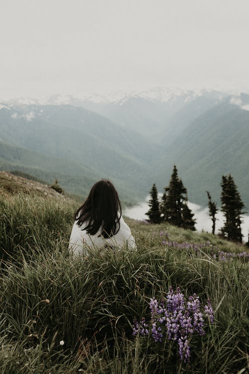 不可识别的女人坐在山上，看着雄伟的山脉 · 免费素材图片