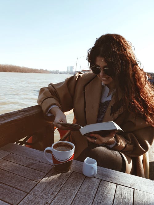 棕色外套坐在棕色木制码头上的女人 · 免费素材图片