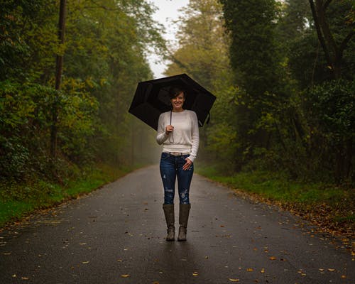 白色上衣和蓝色牛仔牛仔裤，拿着伞走在路上的女人 · 免费素材图片