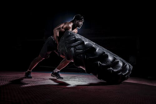 坚强的赤膊黑人在黑暗的健身房里翻转沉重的轮胎 · 免费素材图片