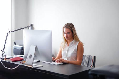 使用macbook空气在棕色的木桌上的白色无袖衬衫的女人 · 免费素材图片