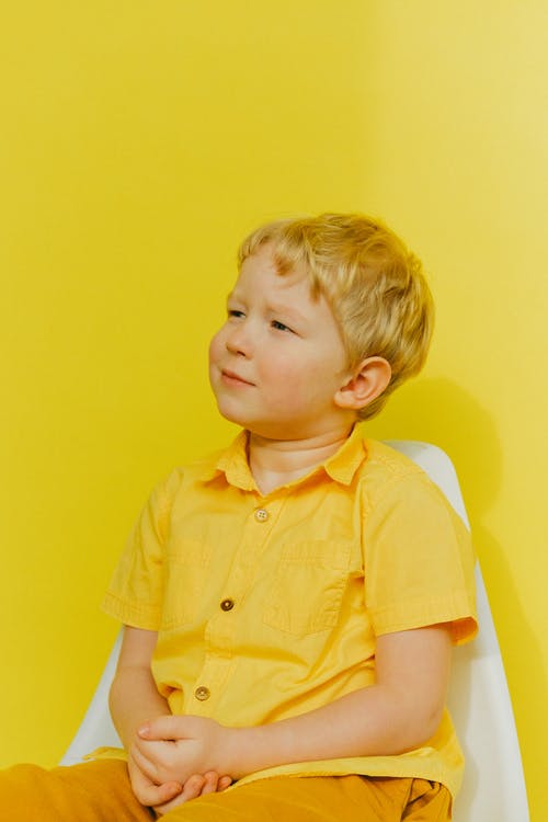 黄色纽扣衬衫坐在墙上的白色椅子上的男孩 · 免费素材图片