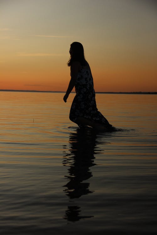 女人在日落时站在水面上的剪影照片 · 免费素材图片