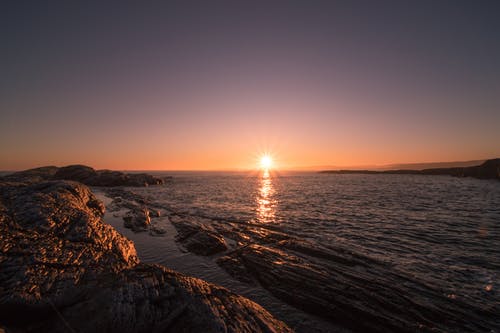 日落期间在水体旁边的棕色岩石 · 免费素材图片