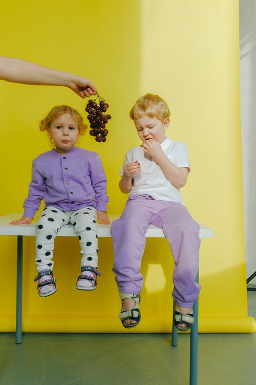 在孩子们坐在桌子上之间抱着葡萄的人 · 免费素材图片
