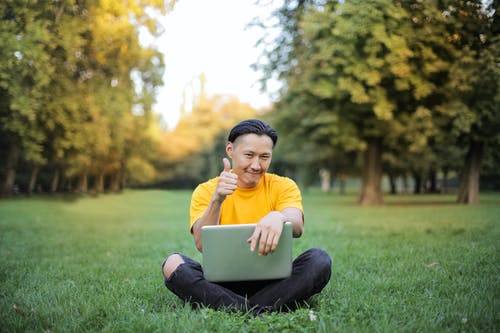黄色乘员脖子上的t恤，坐在草地上使用银macbook的男人 · 免费素材图片
