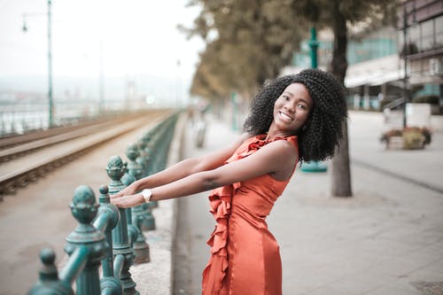 金属栏杆构成的橙色礼服的微笑女人的照片 · 免费素材图片