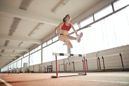 红色运动胸罩跳上白色和黑色障碍的女人 · 免费素材图片