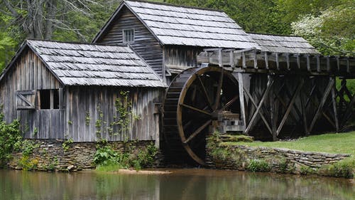 灰色的木制房，四周绿树环绕的水磨坊 · 免费素材图片