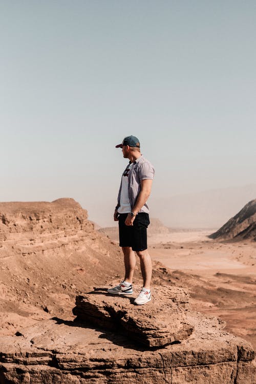 男子站在棕色的岩层上 · 免费素材图片