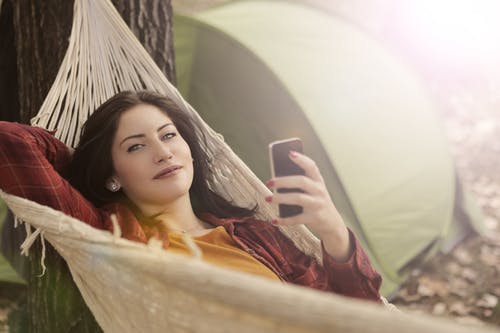 使用手机时躺在吊床上的女人 · 免费素材图片