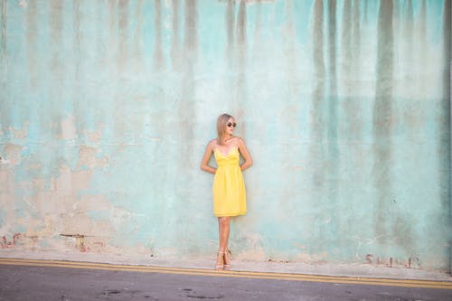 女人穿着黄色的衣服，站在前面的旧蓝色墙看着别处的照片 · 免费素材图片