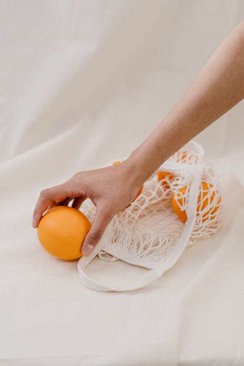 在白色纺织品上持有橙色水果的人 · 免费素材图片