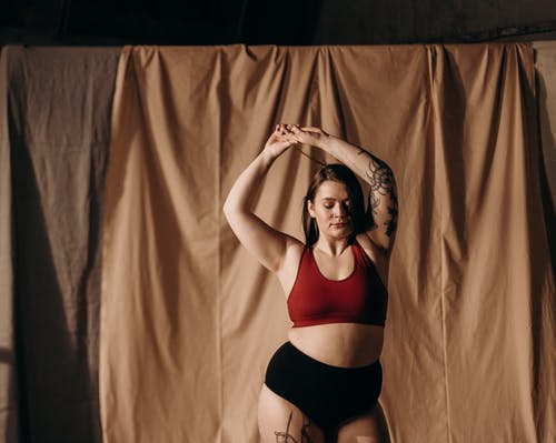 红色运动胸罩和黑色内裤站在棕色的窗帘旁边的女人 · 免费素材图片