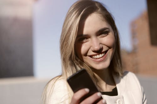 微笑的女士拿着黑色的智能手机 · 免费素材图片
