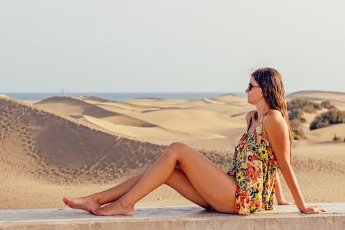 女人坐在沙子在天空的沙滩上 · 免费素材图片