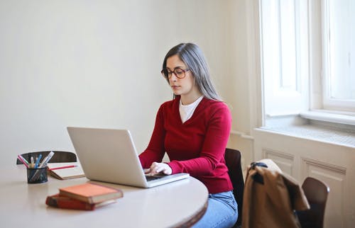 坐在椅子上使用macbook的红色长袖衬衫的女人 · 免费素材图片