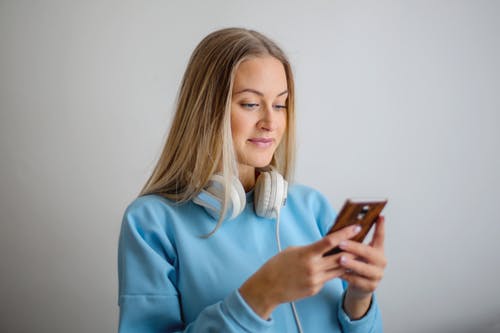 拿着棕色智能手机的蓝色长袖衬衫的女人 · 免费素材图片