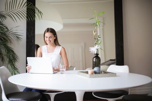 白色无袖连衣裙坐在桌子前与macbook椅子上的女人 · 免费素材图片