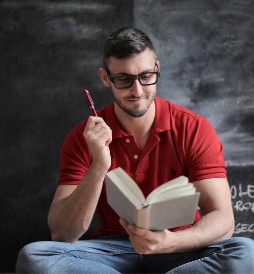红色polo衫和拿着红色钢笔和书的蓝色牛仔牛仔裤的男人 · 免费素材图片