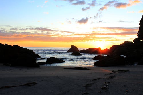 海滩和岩石在橘黄色的夕阳下 · 免费素材图片