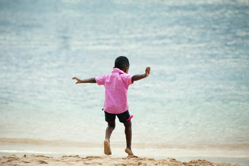 男孩穿着粉红色的衣领的衬衫在海边上运行 · 免费素材图片