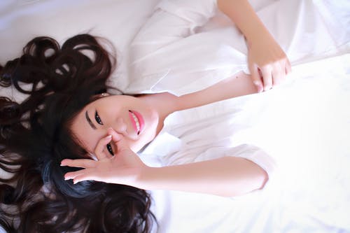 说谎在白色床上的微笑的妇女 · 免费素材图片