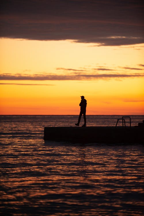 男子站在木码头在日落的剪影 · 免费素材图片