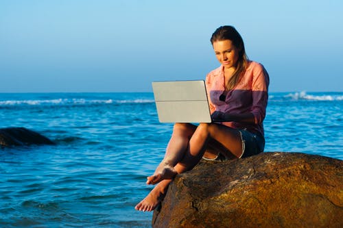 使用笔记本电脑时坐在棕色岩石上的女人 · 免费素材图片