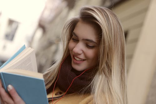 浅焦点女人读一本书时微笑的照片 · 免费素材图片