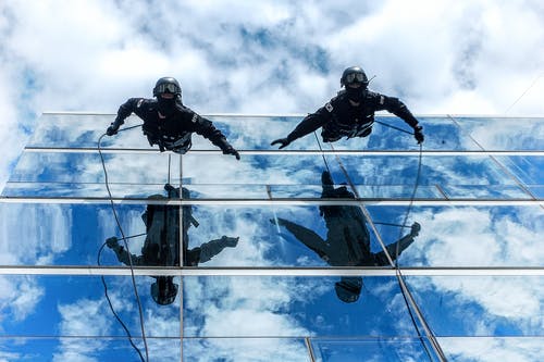 在多云的天空下建筑玻璃墙上的两个人 · 免费素材图片
