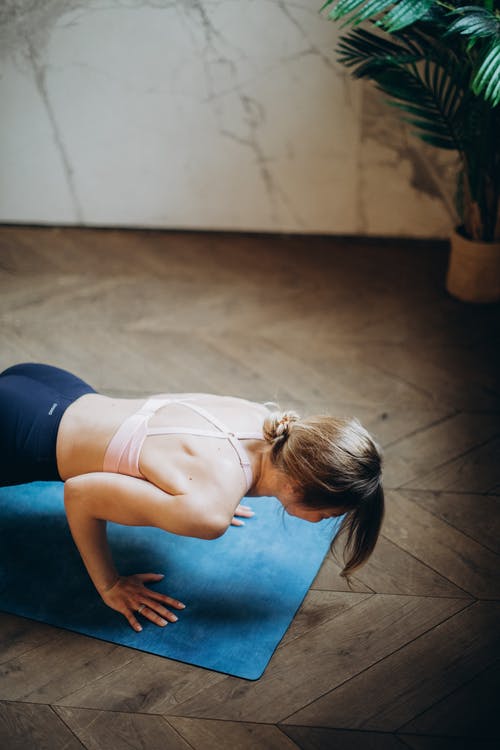 白色背心和黑色紧身裤的女人在蓝色瑜伽垫上弯曲她的身体 · 免费素材图片