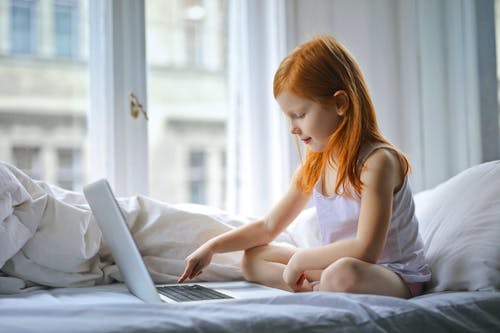 美丽的姑娘坐在白色的床上，用笔记本电脑 · 免费素材图片