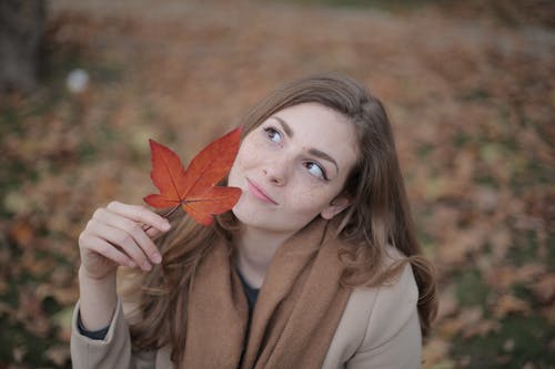 拿着红枫叶的棕色外套的女人 · 免费素材图片