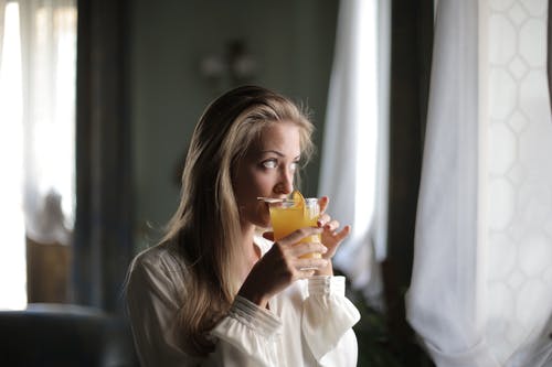 白色的长袖衬衫，喝橙汁的女人 · 免费素材图片