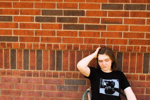 女人穿着黑色t恤，坐在木椅上的砖墙的照片 · 免费素材图片