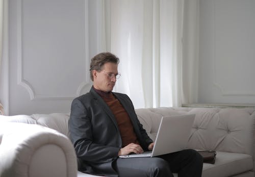 一个男人坐在白色的沙发上，使用笔记本电脑 · 免费素材图片