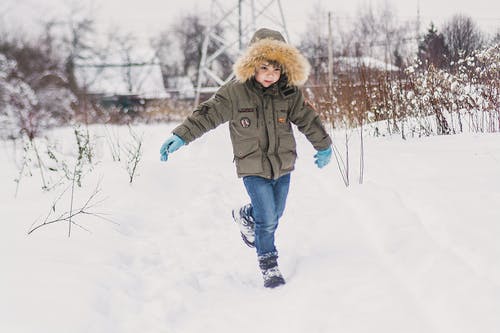 绿色外套和蓝色牛仔牛仔裤，站在积雪的地面上的孩子 · 免费素材图片