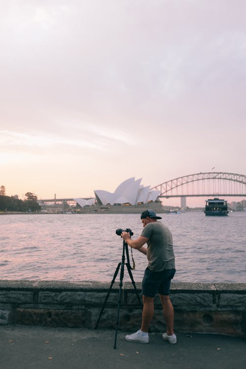 男子在河边的三脚架上设置黑色单反相机 · 免费素材图片